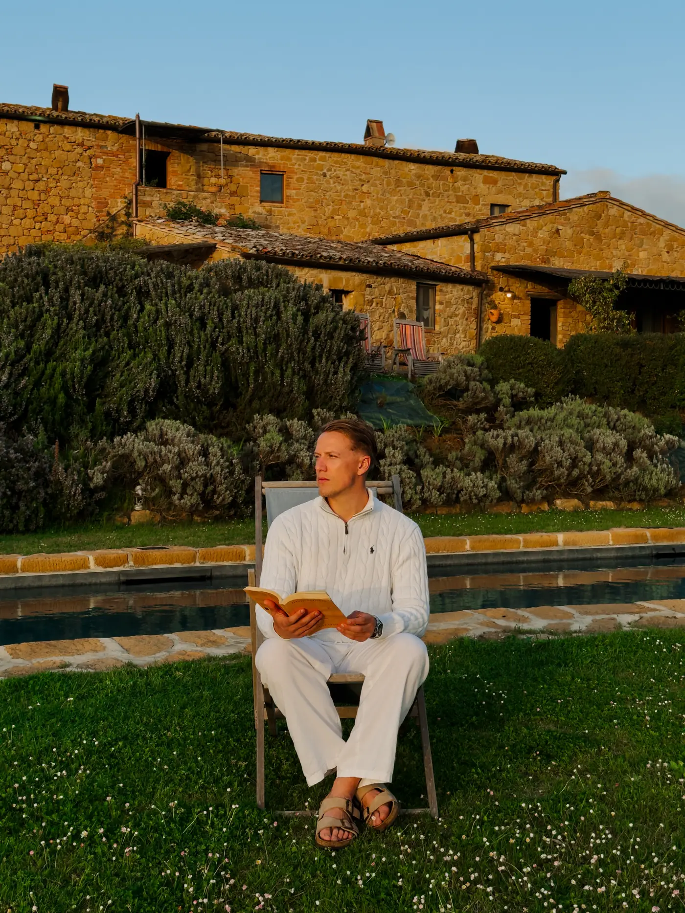 Beni reading in a garden chair in front of a stone farmhouse at golden hour
